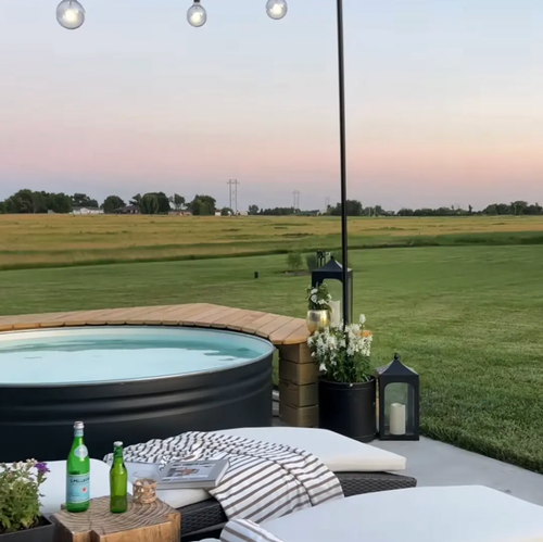 Outdoor stock tank pool on a patio with lounge chairs, string lights, and a large grassy field in the background at dusk in regional australia